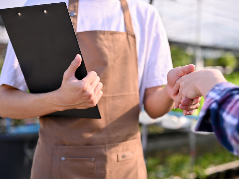 Profesional con portapapeles realizando una verificación de campo y estrechando la mano de un aliado comercial formal.